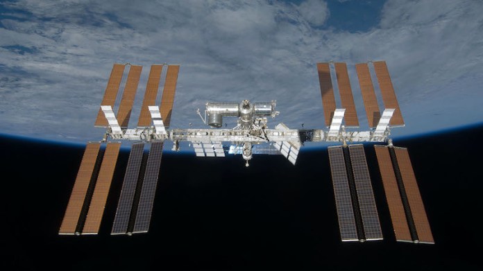 Several connected cylinders with 8 rectangular golden panels on each end floating above Earth.