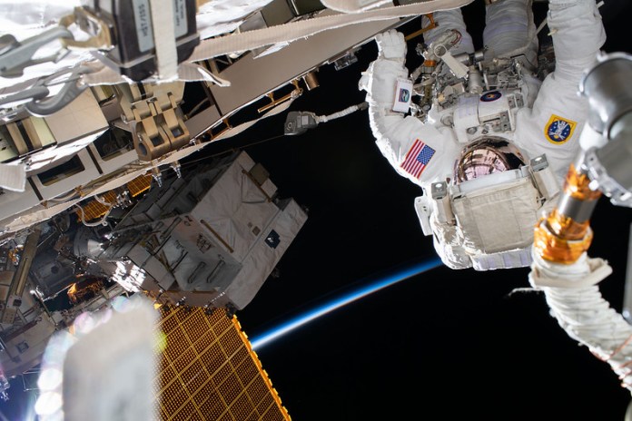 Upside-down astronaut in white space suit with American flag patch outside space station.