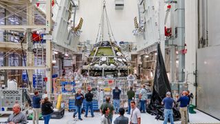 a distant spacecraft in a manufacturing facility surrounded by workers in hard hats