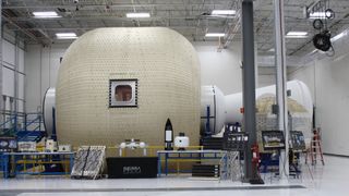 photo of a large, cylindrical tan habitat structure inside a white-walled room