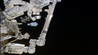 photo of a white space capsule against the blackness of space, with parts of the international space station in the foreground