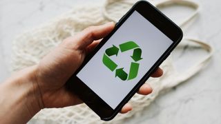 A hand holding a smart phone showing a green recycling symbol.