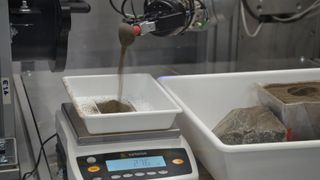 closeup of a scoop pouring dirt onto a digital scale in a laboratory