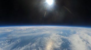 A view of a cure of earth at high altitude against a black sky with a glaring sun peaking out from the top near the center.