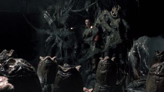 Screenshot from the movie Alien vs. Predator. Three terrified humans have been pasted to a cave wall and are stuck there. Before there is a room full of opening xenomorph eggs. One poor human has a facehugger alien stuck on their face.