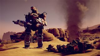 A heavily-armed mech suit in a desert environment, stood next to a smoking wreck.