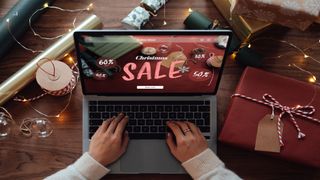 Image is an overhead shot of a woman shopping for Christmas presents online on a laptop