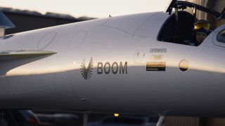 a pilot in a flight helmet sits in a sleek silver jet with a sharp nose cone