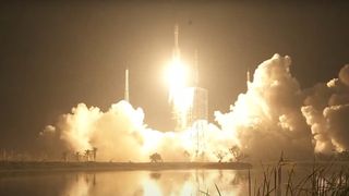 a rocket lifts off at night, creating a large plume of fire beneath it