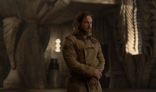 A dusty bearded man stands in a sterile stone room