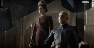 A royal sci-fi figure sits on a throne beside his queen