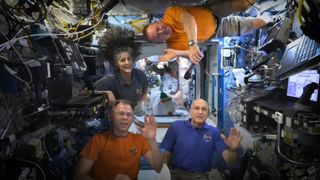 three men and one woman wave from inside the international space station