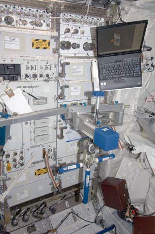 a silver metallic bar with a foam block beside two blue foam handholds. wires connect the arm to a laptop computer