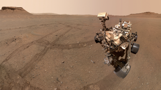 a large mars rover sits in a sandy patch of red planet ground, with some of its tire tracks nearby.