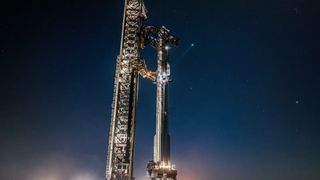 a giant silver rocket stands next to its launch tower at night