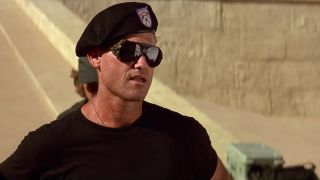 A soldier in a beret and sunglasses standing in front of a wall in the movie Stargate (1994).