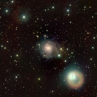 A reddy yellow spiral against a black background punctuated by green and yellow orbs