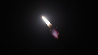 a rocket launches at night above a plume of fire