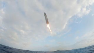 water-level view of a large silver spacecraft coming down for a vertical splashdown in the ocean