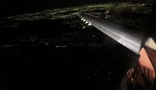 through an airplane window, a wing stretches out into the night, lights of a city below show a slight curvature in the earth.