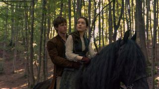 A young woman and man on horseback in a forest