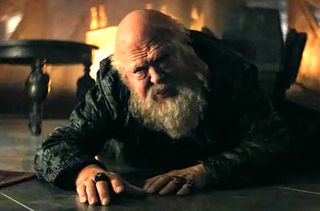 A bearded old man crawls across the floor