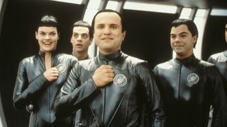 Four humanoid aliens in black leather outfits, smiling naively.