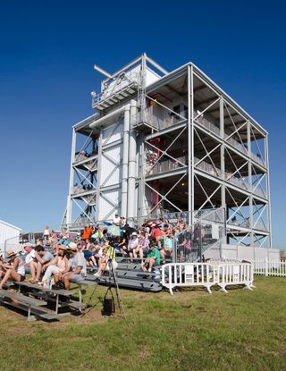 photo of a large metallic gantry, behind a set of bleachers where about 50 people sit