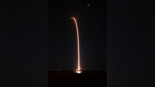 a black-and-white rocket launches at night above a bright plume of fire