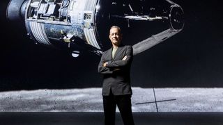 a man in a suit stands with his arms crossed in front of a photo of a spacecraft near the moon