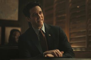 A clean-cut man in a suit sits in a booth in a classy bar